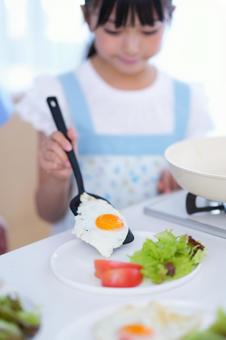 料理を仕上げるエプロン姿の子ども 女の子,目玉焼き,フライ返しの写真素材