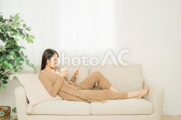 ソファでスマホを使う女性（笑顔） スマホ,スマートフォン,ソファの写真素材
