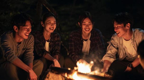 キャンプファイヤーを楽しむ若い男女 キャンプファイヤーを楽しむ若い男女の写真