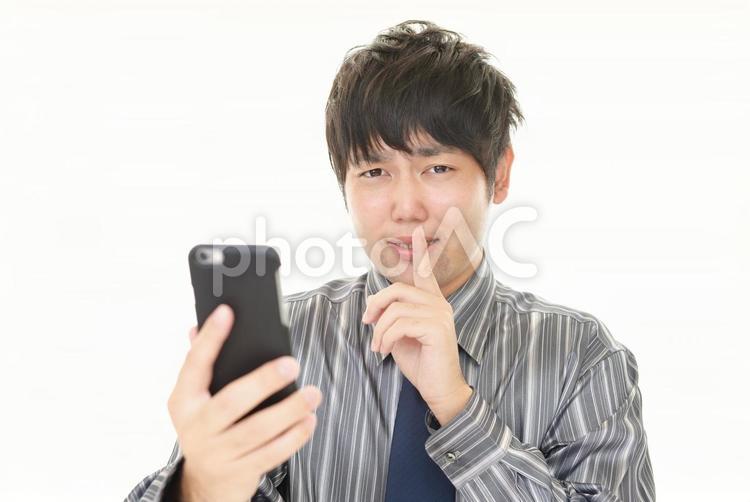 スマホを持って内緒のポーズをとる男性 男性,スマホ,ビジネスの写真素材