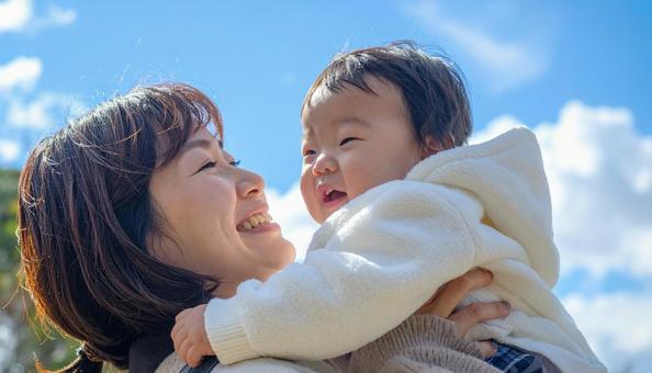 青空の下、子供を抱っこする母親 青空の下、子供を抱っこする母親の写真