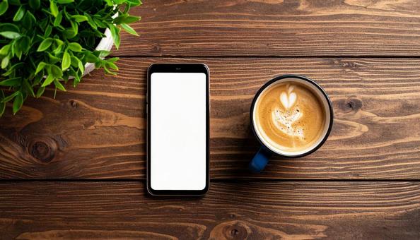 カフェラテとスマホが並ぶデスク風景 カフェラテとスマホが並ぶデスク風景の写真