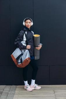 ヨガマットを持ってチラ見する女性 ヨガマットを持ってチラ見する女性 女性,ヘッドフォン,人物の写真素材