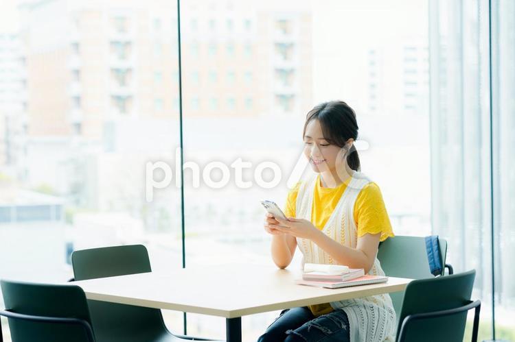 カフェでスマホを見る学生 スマホ,若い女性,笑顔の写真素材