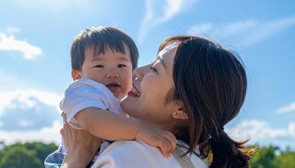 青空の下、子供を抱っこする母親 青空の下、子供を抱っこする母親の写真