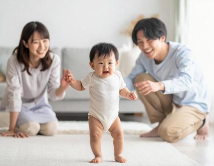 初めて歩いた赤ちゃんと見守る若い両親 初めて歩いた赤ちゃんと見守る若い両親の写真