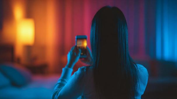 光に包まれた空間で、スマホを構える女性の写真