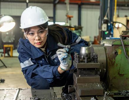工場で加工機械で金属加工する女性スタッフ 工場で加工機械で金属加工する女性スタッフの写真