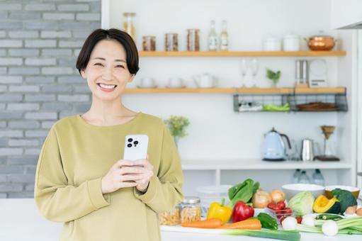 キッチンでスマホを持つミドルの女性 キッチンでスマホを持つミドルの女性の写真