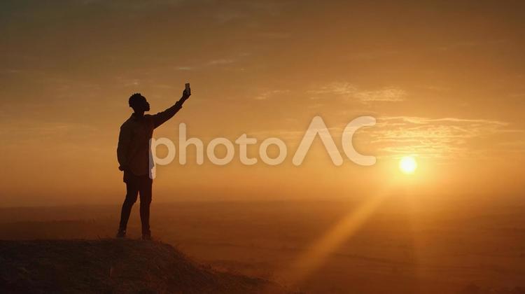 山頂で夕日を望む男性 男性,シルエット,夕焼けの写真素材