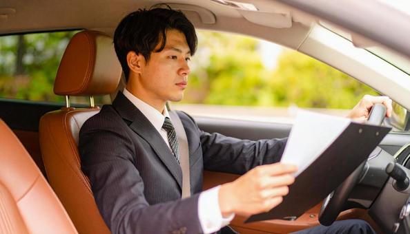手もとに書類を持って運転するサラリーマン 手もとに書類を持って運転するサラリーマンの写真