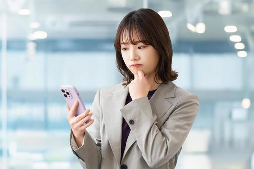 スマホを見て考える女性・ビジネスウーマン スマホを見て考える女性・ビジネスウーマン 女性,困る,考えるの写真素材