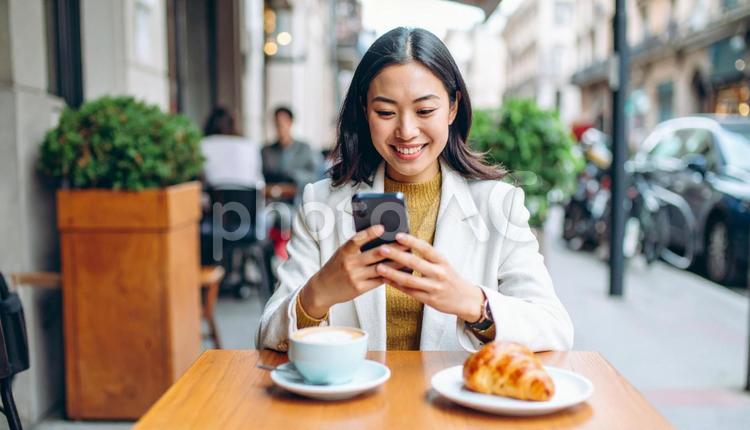 カフェで携帯を使う若いビジネスウーマン　 アプリ,sns,スマートフォンの写真素材