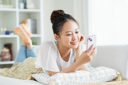 リビングでスマホを見る若い女性 リビングでスマホを見る若い女性 スマートフォン,笑顔,女性の写真素材