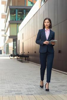 街なかでタブレットを持って歩くパンツスーツの女性 ビジネスウーマン,ビジネス,女性の写真素材