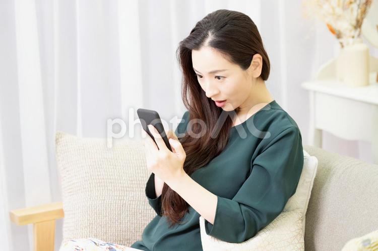 リビングのソファーに座ってスマホを操作する主婦 スマホ,ソファー,女性の写真素材