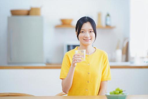 カメラ目線でコップを持つ黄色い服の女性の写真