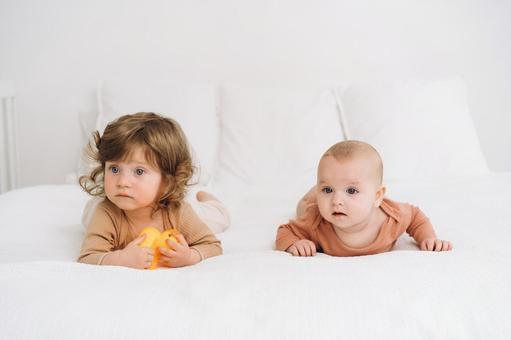うつ伏せで何かを見つめる2人の子供 赤ちゃん,かわいい,ベッドの写真素材