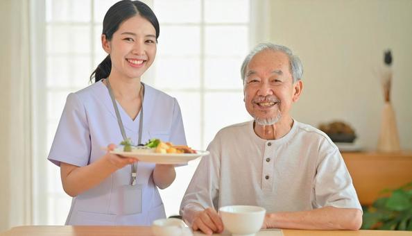 笑顔で食事を運ぶ女性介護士と高齢男性 笑顔で食事を運ぶ女性介護士と高齢男性の写真