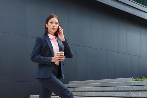 オフィスビルの外の階段でコーヒー片手に電話しているアジア人女性 ビジネスウーマン,ビジネス,女性の写真素材