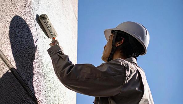 住宅の外壁塗装をする作業服の男性の写真