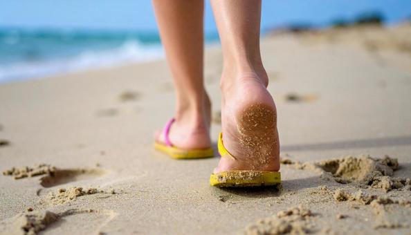 夏の終わり　砂浜をサンダルで歩く女の子の写真