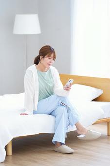ベッドに座りスマホを見る女性の写真