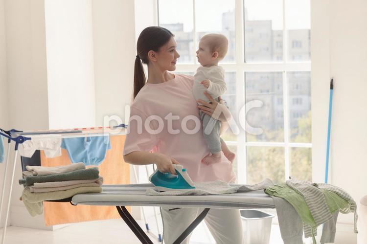 赤ちゃんを抱っこしてアイロンする女性と太陽 親子,女性,人物の写真素材