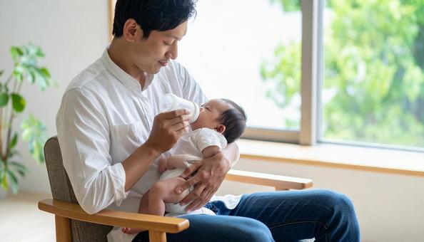 椅子に座り赤ちゃんに哺乳瓶で授乳する父親 椅子に座り赤ちゃんに哺乳瓶で授乳する父親の写真