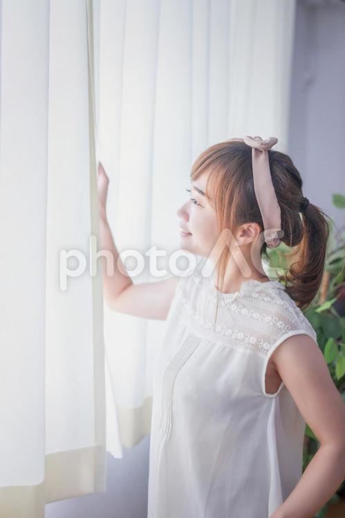カーテンから差し込む朝日を浴びる若い女性 換気,窓,朝日の写真素材