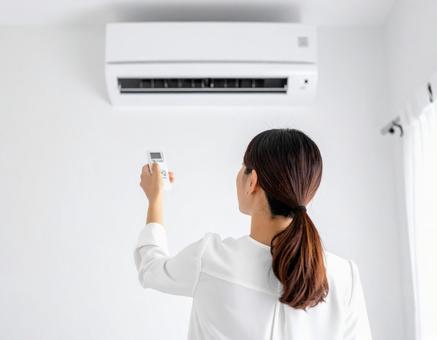 エアコンをリモコンで操作する女性の後ろ姿 エアコンをリモコンで操作する女性の後ろ姿の写真