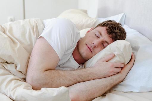 ベッドで横向きで寝る男性の写真