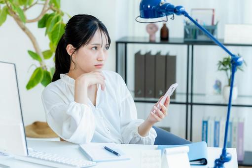 スマホを見ながら考えるビジネスウーマン スマホ,考える,悩むの写真素材