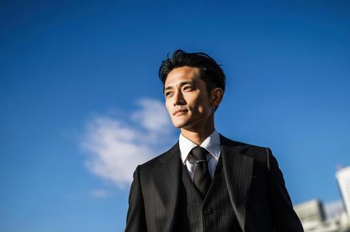 青空を見上げる若いスーツ姿のビジネスマンの写真