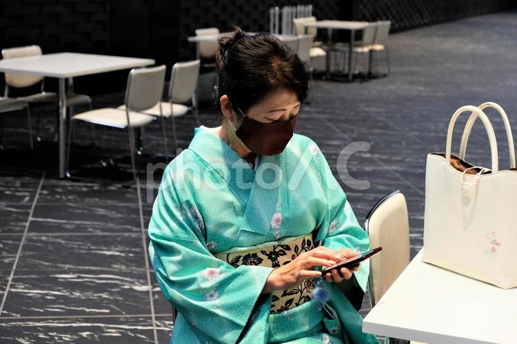 オフィスビルの無料開放広場の椅子に座ってスマホ操作をする着物の女性 着物,和服,女性の写真素材