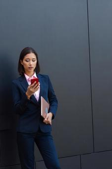 オフィスビルの外でタブレットを抱えながらスマートフォンを見ているビジネスウーマン ビジネスウーマン,ビジネス,女性の写真素材