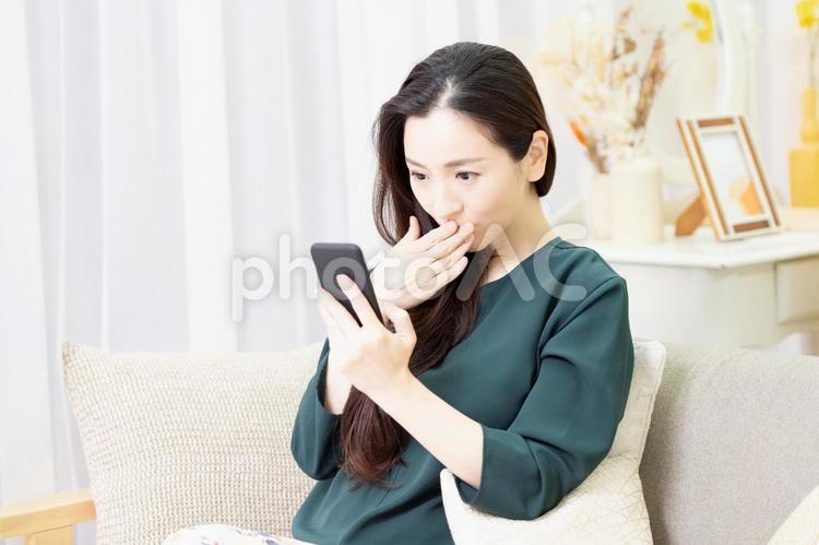 リビングのソファーに座ってスマホを操作する主婦 スマホ,ソファー,女性の写真素材