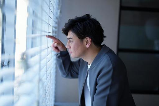 ブラインドの隙間から覗く男性 ブラインドの隙間から覗く男性の写真