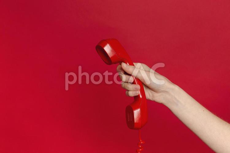 赤い電話の受話器を持っている人の手元 手元,赤,受話器の写真素材