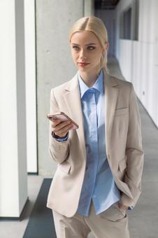 オフィスの通路でスマートフォンを持って立つビジネスウーマン ビジネスウーマン,ビジネス,女性の写真素材