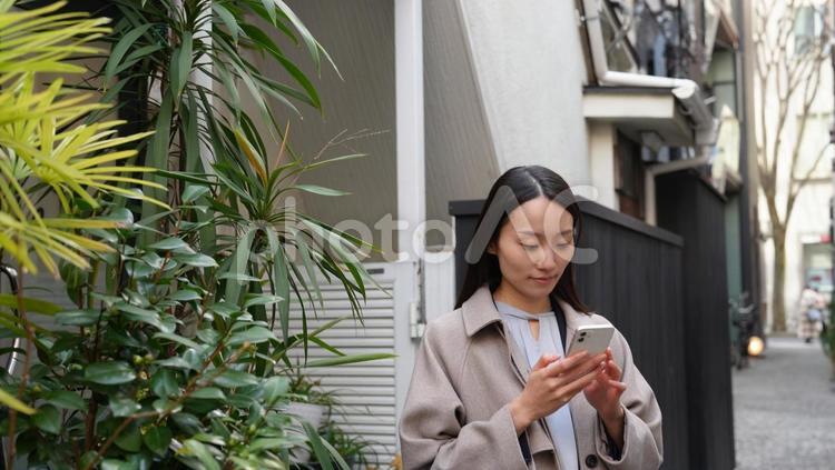 路地で待ち合わせをしスマホを操作する女性 女性,待ち合わせ,黒髪の写真素材
