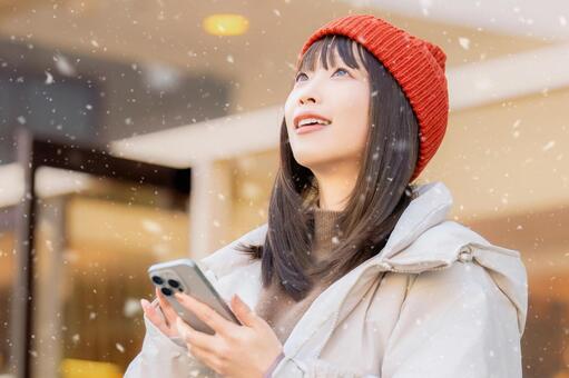 雪の降る冬の街角でスマホを使う女性 冬,雪,女性の写真素材
