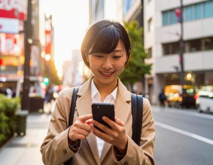 オフィス街でスマホを操作する女性社員 オフィス街でスマホを操作する女性社員の写真