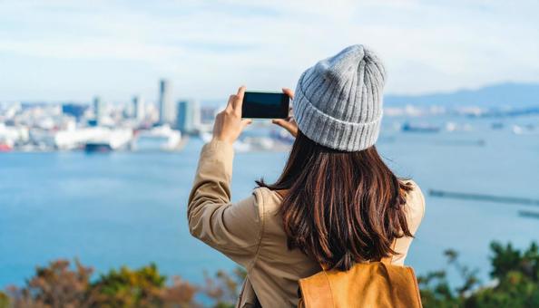 海の向こうを携帯で撮影する観光客の女性 海の向こうを携帯で撮影する観光客の女性の写真
