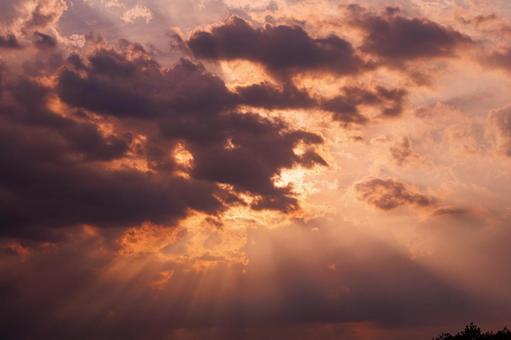 夕暮れ時の雲の間から漏れる夕日の光芒の写真