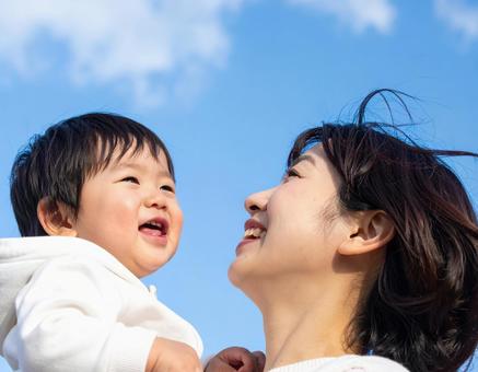 青空の下、子供を抱っこする母親 青空の下、子供を抱っこする母親の写真