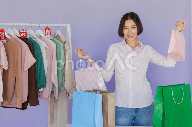 セールのタグの付いたハンガーに掛かった洋服と紙袋を持っている女性 セール,ショップ,女性の写真素材