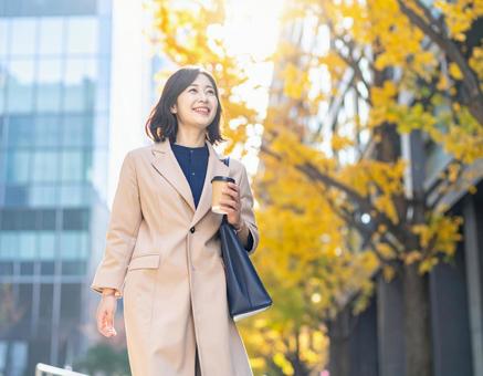 オフィス街を笑顔で歩く通勤中の女性の写真