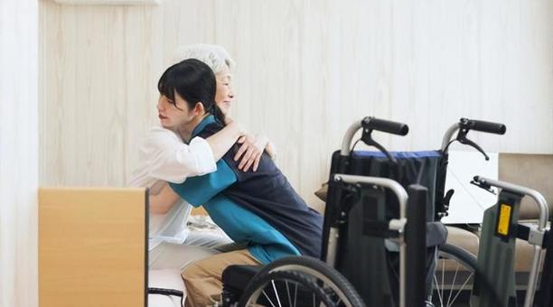 高齢者の移乗介助をするアジア人介護士 高齢者の移乗介助をするアジア人介護士の写真