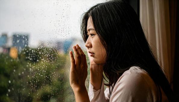 困った顔で窓の外を見る若い女性の写真